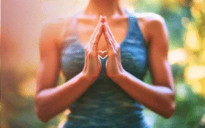 Mulher com as mãos juntas. Natureza ao fundo.